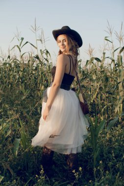 Bir kovboy kız günbatımında bir çiftçinin ürün alan Mısır standları ve samanlık dinlenme gibi genç bir kadın giyinmiş