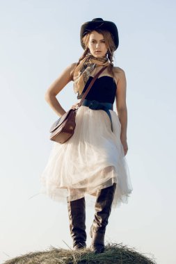 Bir kovboy kız günbatımında bir çiftçinin ürün alan Mısır standları ve samanlık dinlenme gibi genç bir kadın giyinmiş