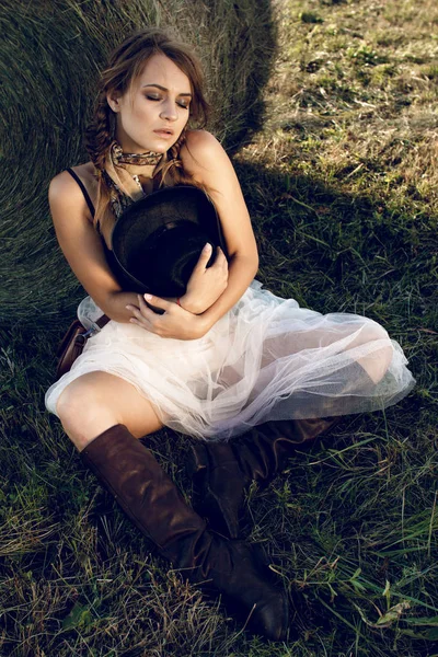 Bir kovboy kız günbatımında bir çiftçinin ürün alan Mısır standları ve samanlık dinlenme gibi genç bir kadın giyinmiş