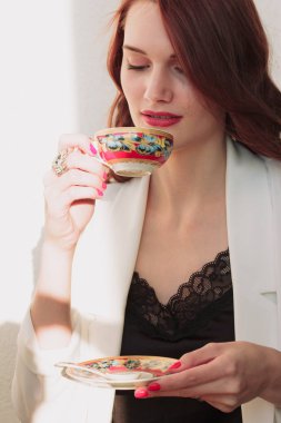 Güzel redhear kadın beyaz ceket, yüksek topuklu ve siyah gömlek balcone oturan