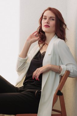 Güzel redhear kadın beyaz ceket, yüksek topuklu ve siyah gömlek balcone oturan