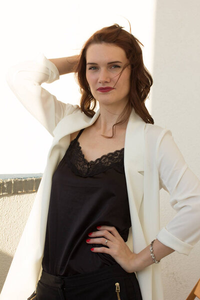 Beautiful redhear woman white jacket, high heels, and black shirt sitting the balcone