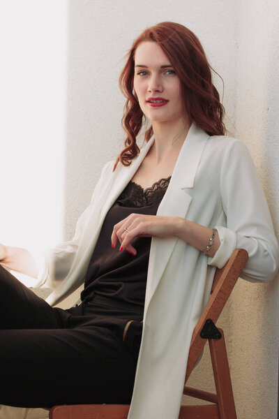 Beautiful redhear woman white jacket, high heels, and black shirt sitting the balcone