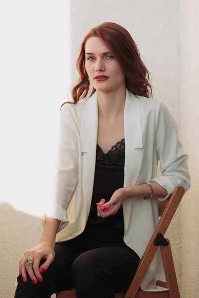 Beautiful redhear woman white jacket, high heels, and black shirt sitting the balcone