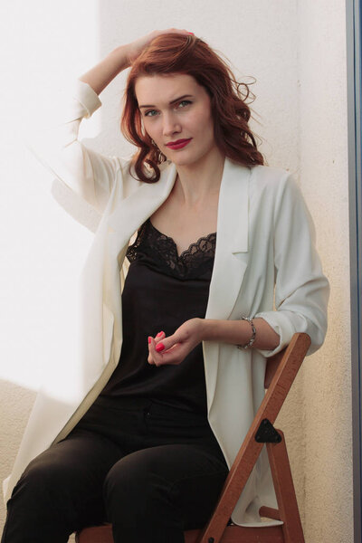 Beautiful redhear woman white jacket, high heels, and black shirt sitting the balcone