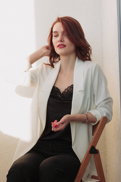 Beautiful redhear woman white jacket, high heels, and black shirt sitting the balcone