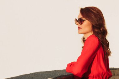 Kırmızı bir elbise ve güneş gözlüğü gün batımında balkonda genç kız esmer ayakta