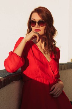 Kırmızı bir elbise ve güneş gözlüğü gün batımında balkonda genç kız esmer ayakta