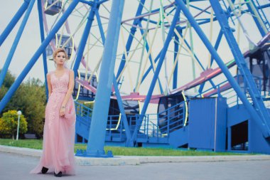 Uzun pembe gece elbisesi yolu Park'ta yürüyordunuz genç güzel kadın. Moda stil açık havada dönme dolap yakınındaki güzel güzel kız portresi