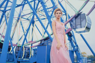 Uzun pembe gece elbisesi yolu Park'ta yürüyordunuz genç güzel kadın. Moda stil açık havada dönme dolap yakınındaki güzel güzel kız portresi