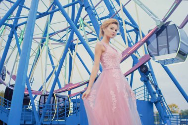 Uzun pembe gece elbisesi yolu Park'ta yürüyordunuz genç güzel kadın. Moda stil açık havada dönme dolap yakınındaki güzel güzel kız portresi