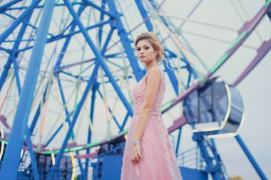 Uzun pembe gece elbisesi yolu Park'ta yürüyordunuz genç güzel kadın. Moda stil açık havada dönme dolap yakınındaki güzel güzel kız portresi