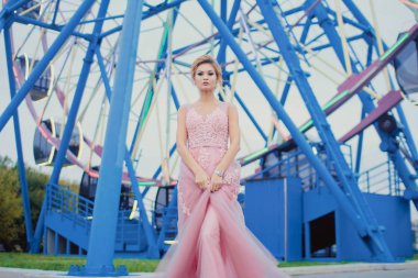 Uzun pembe gece elbisesi yolu Park'ta yürüyordunuz genç güzel kadın. Moda stil açık havada dönme dolap yakınındaki güzel güzel kız portresi