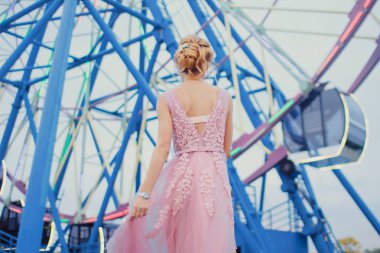 Uzun pembe gece elbisesi yolu Park'ta yürüyordunuz genç güzel kadın. Moda stil açık havada dönme dolap yakınındaki güzel güzel kız portresi