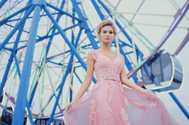 Uzun pembe gece elbisesi yolu Park'ta yürüyordunuz genç güzel kadın. Moda stil açık havada dönme dolap yakınındaki güzel güzel kız portresi