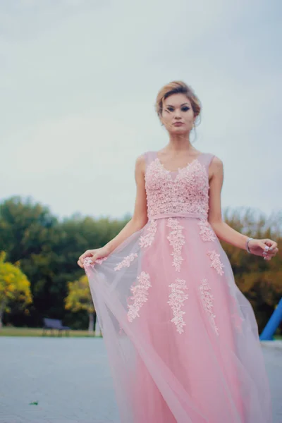Uzun pembe gece elbisesi yolu Park'ta yürüyordunuz genç güzel kadın. Moda stil açık havada dönme dolap yakınındaki güzel güzel kız portresi