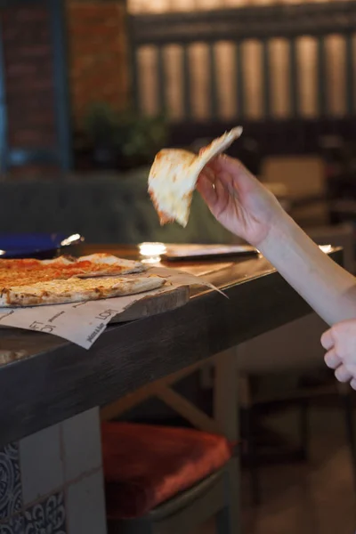 Casual girl eating pizza in the restaurant and enjoying this. Funny blonde girl in white t-shirt eating pizza at restaurant