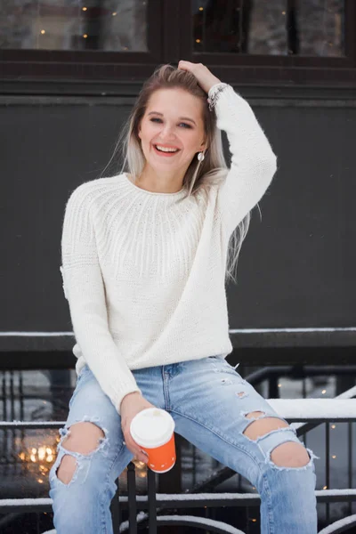 Beautiful natural young smiling shy friendly blonde woman wearing knitted sweater on a grey background.