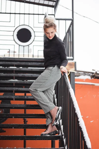 Stylish young woman in boots sitting on stairs. Winter style