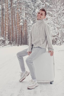 Bavul ve gitmek yolu çam ormanı tutan karda yürüme beyaz giysili genç moda adam portresi. Kış tatil seyahat kavramı. Kışın açık havada. Kayak Merkezi, Kayak resort montaj