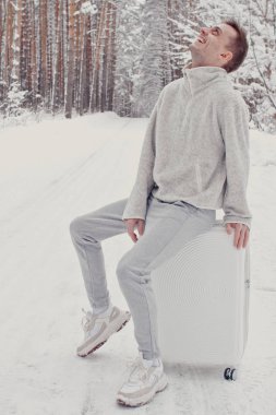 Bavul ve gitmek yolu çam ormanı tutan karda yürüme beyaz giysili genç moda adam portresi. Kış tatil seyahat kavramı. Kışın açık havada. Kayak Merkezi, Kayak resort montaj