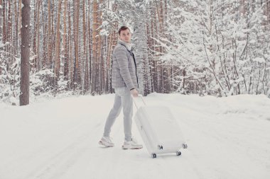 Bavul ve gitmek yolu çam ormanı tutan karda yürüme beyaz giysili genç moda adam portresi. Kış tatil seyahat kavramı. Kışın açık havada. Kayak Merkezi, Kayak resort montaj