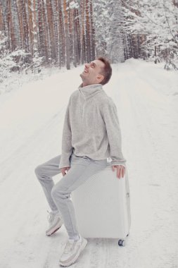 Bavul ve gitmek yolu çam ormanı tutan karda yürüme beyaz giysili genç moda adam portresi. Kış tatil seyahat kavramı. Kışın açık havada. Kayak Merkezi, Kayak resort montaj
