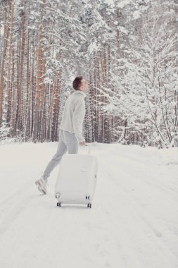 Bavul ve gitmek yolu çam ormanı tutan karda yürüme beyaz giysili genç moda adam portresi. Kış tatil seyahat kavramı. Kışın açık havada. Kayak Merkezi, Kayak resort montaj