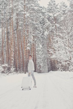 Bavul ve gitmek yolu çam ormanı tutan karda yürüme beyaz giysili genç moda adam portresi. Kış tatil seyahat kavramı. Kışın açık havada. Kayak Merkezi, Kayak resort montaj