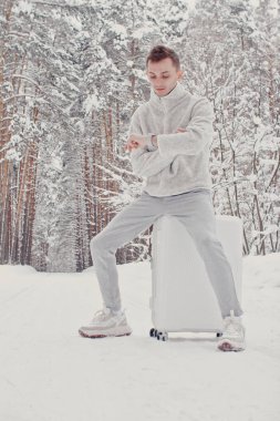 Bavul ve gitmek yolu çam ormanı tutan karda yürüme beyaz giysili genç moda adam portresi. Kış tatil seyahat kavramı. Kışın açık havada. Kayak Merkezi, Kayak resort montaj