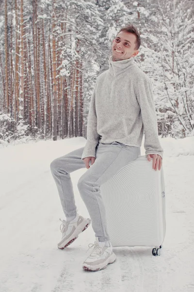 Bavul ve gitmek yolu çam ormanı tutan karda yürüme beyaz giysili genç moda adam portresi. Kış tatil seyahat kavramı. Kışın açık havada. Kayak Merkezi, Kayak resort montaj