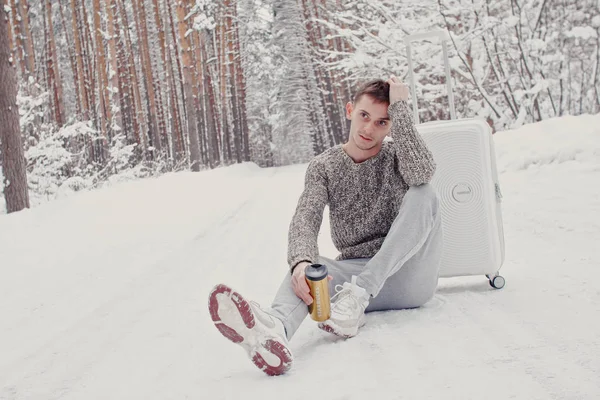 Portret Młodzieńca Modne Białe Szaty Siedząc Śniegu Trzyma Walizkę Iść — Zdjęcie stockowe