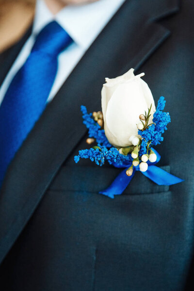 White rose and blue delphinium boutonniere flower on groom's wedding coat with blue tie