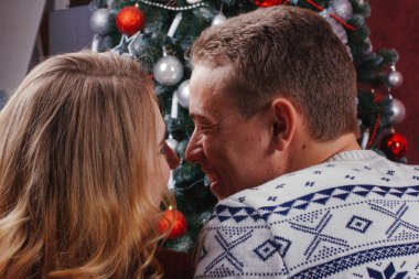 Birkaç aşk bir Noel ağacının yanında oturan, sıcak kazak giyiyor, sarılmak ve uzak kamera ağaca doğru bakıyor.