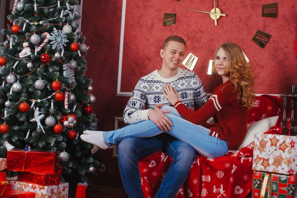 Jovens felizes dão presentes uns aos outros perto da lareira perto da árvore de Natal. Os amantes casal estão cheios de expectativa para o ano novo — Fotografia de Stock