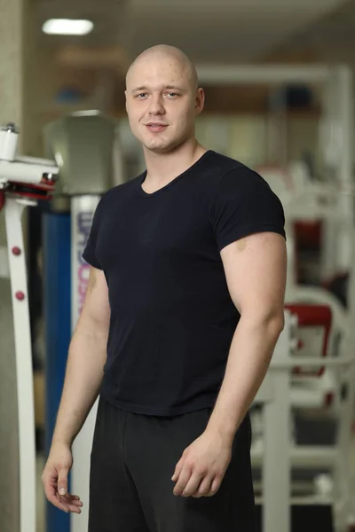 Sporty man in black sportswear. Young guy wearing t-shirt and relaxing in gym. Workout and break concept. Handsome sportsman bodybuilder with an ideal body, after coaching poses in front of the camera