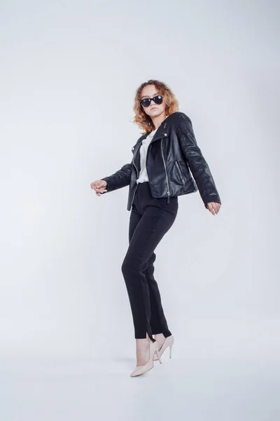 Mujer sensual de moda bastante joven posando sobre fondo blanco con un traje de chaqueta de cuero estilo hipster. Elegante chica de moda hipster en ropa negra y camisa blanca . — Foto de Stock