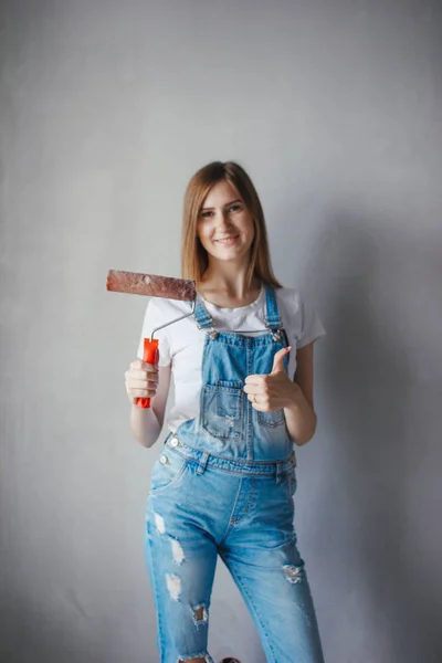 Enfoque selectivo en rodillo de pintura en la mano joven mujer caucásica delante de una nueva pared de reparación en una habitación . —  Fotos de Stock