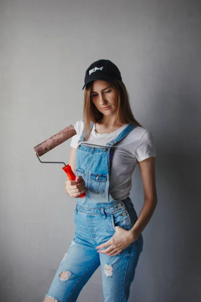 Enfoque selectivo en rodillo de pintura en la mano joven mujer caucásica delante de una nueva pared de reparación en una habitación . —  Fotos de Stock