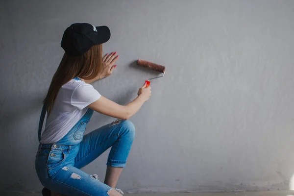 Selective focus at painting roller in young Caucasian woman hand in front of a reparing new wall in a room. — Stock Photo, Image