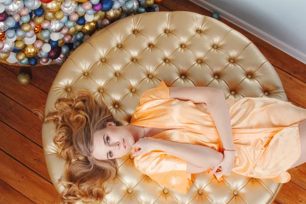 Beautiful blonde woman in peach silk robe laying on the round pouf. View from top, high angle — Stock Photo, Image