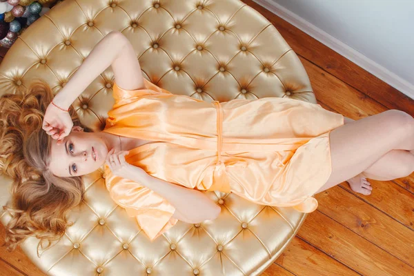 Красива блондинка в персиковому шовковому халаті, що лежить на круглому пуфі. Вид зверху, високий кут — стокове фото