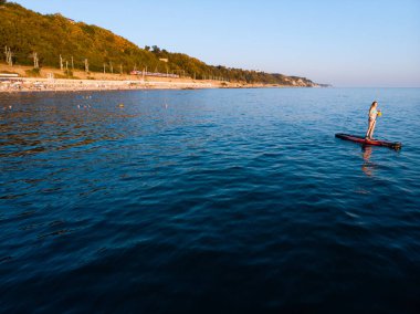 Stand Up Paddle tahtasında çekici bir kadın yemek masasında kürek çeken ve şeffaf suyun tadını çıkaran bir kadın. Tropik seyahat, seyahat tutkusu ve su aktivitesi konsepti. Gün batımı ve rahatlama