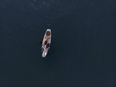 Stand Up Paddle tahtasında çekici bir kadın yemek masasında kürek çeken ve şeffaf suyun tadını çıkaran bir kadın. Tropik seyahat, seyahat tutkusu ve su aktivitesi konsepti. Gün batımı ve rahatlama