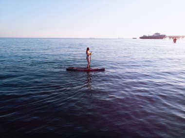 Stand Up Paddle tahtasında çekici bir kadın yemek masasında kürek çeken ve şeffaf suyun tadını çıkaran bir kadın. Tropik seyahat, seyahat tutkusu ve su aktivitesi konsepti. Gün batımı ve rahatlama