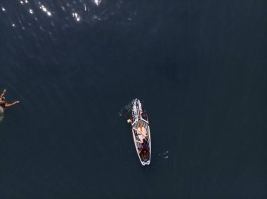 Stand Up Paddle tahtasında çekici bir kadın yemek masasında kürek çeken ve şeffaf suyun tadını çıkaran bir kadın. Tropik seyahat, seyahat tutkusu ve su aktivitesi konsepti. Gün batımı ve rahatlama