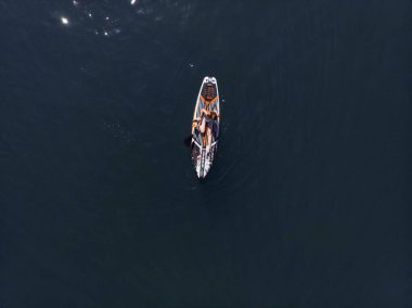 Stand Up Paddle tahtasında çekici bir kadın yemek masasında kürek çeken ve şeffaf suyun tadını çıkaran bir kadın. Tropik seyahat, seyahat tutkusu ve su aktivitesi konsepti. Gün batımı ve rahatlama