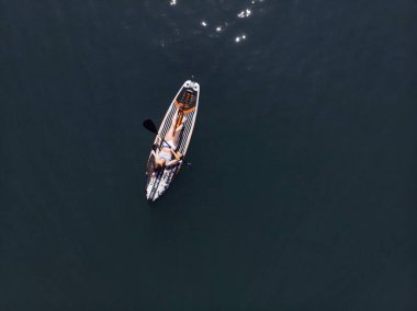 Stand Up Paddle tahtasında çekici bir kadın yemek masasında kürek çeken ve şeffaf suyun tadını çıkaran bir kadın. Tropik seyahat, seyahat tutkusu ve su aktivitesi konsepti. Gün batımı ve rahatlama