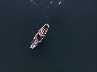 Stand Up Paddle tahtasında çekici bir kadın yemek masasında kürek çeken ve şeffaf suyun tadını çıkaran bir kadın. Tropik seyahat, seyahat tutkusu ve su aktivitesi konsepti. Gün batımı ve rahatlama