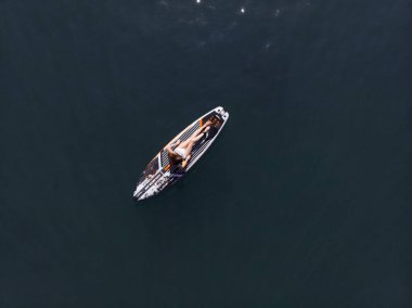 Stand Up Paddle tahtasında çekici bir kadın yemek masasında kürek çeken ve şeffaf suyun tadını çıkaran bir kadın. Tropik seyahat, seyahat tutkusu ve su aktivitesi konsepti. Gün batımı ve rahatlama